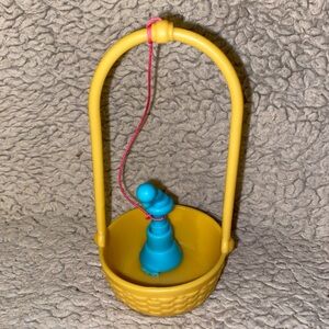 The small turquoise hand-cranked device inside a yellow basket with a handle.